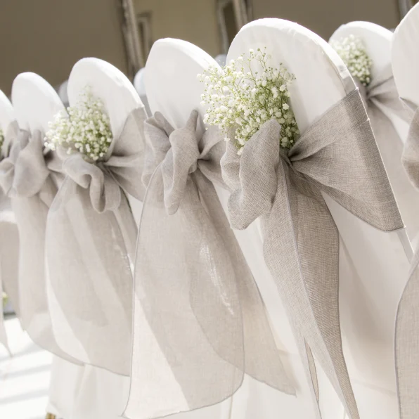 A row of white chairs with grey bows on them.